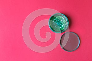 Opened jar with aloe vera lotion on red colored paper background. top view with copy space