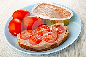 Opened jar with liver pate, sandwich from bread with liver pate and tomato in plate on wooden table