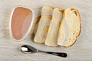 Opened jar with liver pate, slices bread, spoon on wooden table. Top view