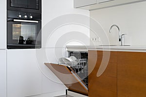 Opened modern dishwasher machine with plates and cups on kitchen