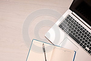 Opened notebook with black pen and silver laptop on a white wooden table, top view, copy spase