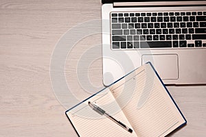 Opened notebook with black pen and silver laptop on a white wooden table, top view, copy spase