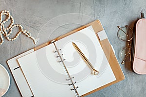 Opened notebook with clean sheets, gold pen, rosary, pink colored case and cup of tea near vase