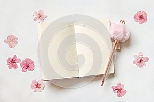 Opened notebook, decorative fur pen and dried pink sakura flowers on white top view, textbook mockup