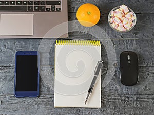 Opened the notebook, laptop, fountain pen, marshmallows, mouse and orange on a dark wooden table. Workplace at home.