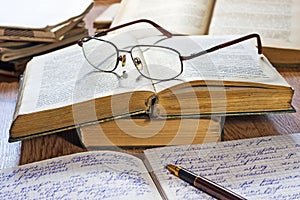 Opened notebook, pen, books and glasses