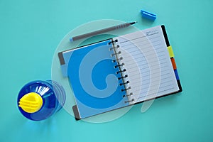 Opened notebook with pen and water bottle on blue background