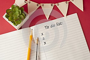 Opened organizer with a to do list inscription, white blank paper pages. Work table with decorative succulent and office supplies