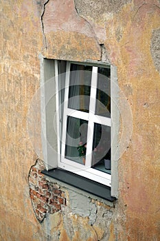 An opened plastic window on bad condition house wall covered with plaster side view vertical closeup