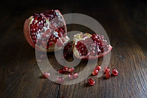 Opened pomegranate fruit with red juicy seeds on rustic wood, dark and moody style, copy space