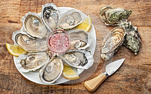 Opened raw oysters with sauce and lemon slices on plate on wooden table. Top view