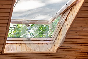 Opened roof window with blinds or curtain in wooden house attic. Room with slanted ceiling made of natural eco materials