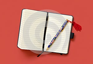 Opened ruled notebook with a ethnic pen on red table top view. Textbook mockup