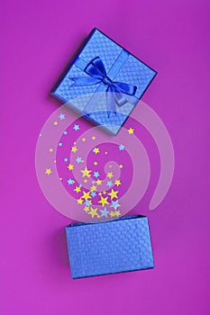 Opened shiny classic blue gift box with satin bow and magic confetti in the shape of stars as attributes of part