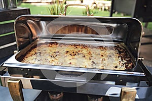 Opened stainless hotel pans on food warmer with baked meal. Self-service buffet table. Celebration, party, birthday or