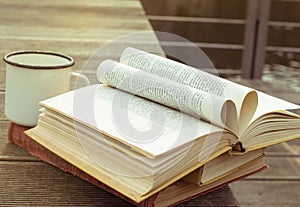 Opened vintage book on the wooden table with old fashioned cup of tea. The page in the form of heart. Side view. The toning.