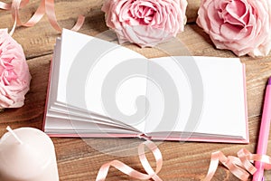 Opened white empty blank notepad, gentle, pink roses, candle, pen, ribbon on old wooden table.