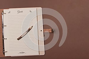 Opened wooden guests book with pen ready to write on brown colored paper background. Top view with copy space