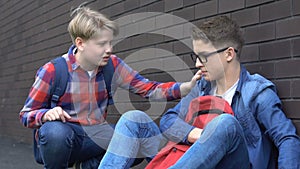 Openhearted schoolboy comforting bullying victim in schoolyard, social problem