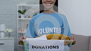 Openhearted young woman holding box with donated clothing, homeless care center