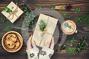 Opening Christmas present. Woman's hands holding decorated gift box on rustic wooden table. Overhead, flat lay, top view