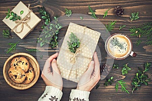 Opening Christmas present. Womans hands holding decorated gift box on rustic wooden table. Overhead, flat lay, top view