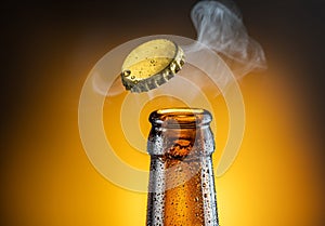 Opening of cold beer bottle - gas output and bottle cap in the air. Isolated on a yellow background