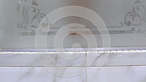 Opening the glass translucent door of the shower, a on a tray of tile tiles