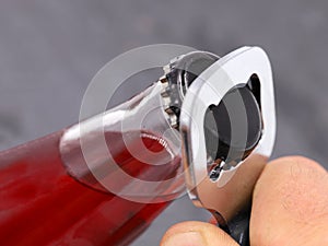 opening red drink bottle with bottle opener on grey background, close up