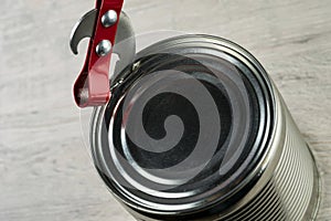 Opening a tin with a can opener. The can opener is on the tin can.