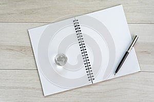 Opening white blank paper note book with pen on the right and decoration glass globe on light grey wooden table background with