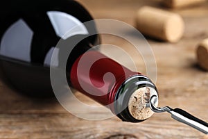 Opening wine bottle with corkscrew on wooden table, closeup