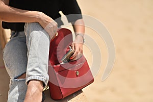 Opening a woman`s bag. Sexy young woman on black t-shirt, fashion sunglasses and blue jeans opens up a red fashion bag