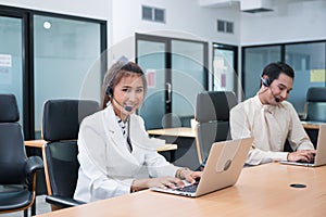 Operator asian woman agent with headset working with laptop on customer consultation in the office with colleague at workplace