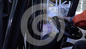 Operator controls loader sitting behind wheel driving past the shelves with goods in warehouse