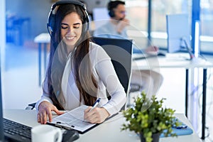 Operator woman wearing headset, multi-tasking by taking notes and listening to Client& x27;s needs in Call Center office