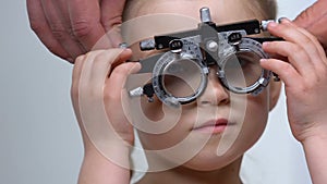 Ophthalmologist helping small girl put on phoropter, eyesight checkup diagnostic