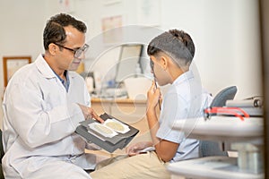 Ophthalmologist or optical staff use book of color blindness test with Indian boy to test for continue the process in optical shop