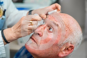 Ophthalmologist pouring drops to dilate the pupil to a man