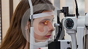 Ophthalmology treatment - a young woman checking her visual acuity with a light of special big optometry machine