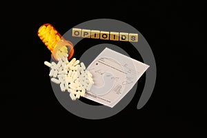 Opioid crisis spelled out on a black background with spilled prescription pills on a prescription pad