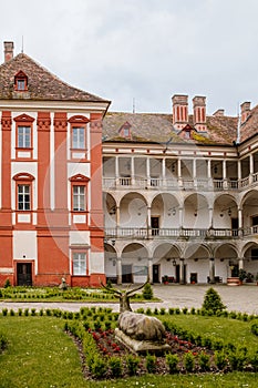 Opocno castle, renaissance chateau, courtyard with arcades and red facade, green lawn with statue and flowers in foreground, sunny