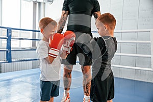 Opponents looking in each other`s eyes before the round starts. Young tattooed coach teaching the kids boxing techniques