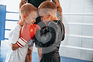 Opponents looking in each other`s eyes before the round starts. Young tattooed coach teaching the kids boxing techniques