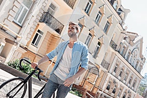 Opportunities don`t happen. You create them. Young brown-haired man standing outdoors with a bicycle and looking away.