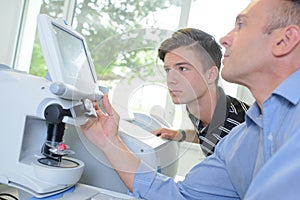 Optician and apprentice using machinery
