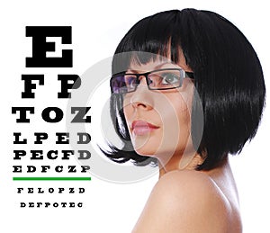 Optician. Beautiful brunette wearing glasses and Snellen eye exam chart isolated on white photo