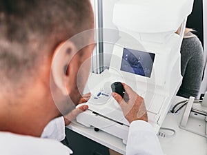 Optician checking his patient`s eye on a machine.