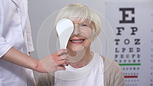 Optician closing elderly ladies eye, maintaining satisfactory eyesight, test