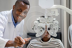 Optician Doing Optometry Eye Exam For Black African teen girl Patient. Male optometrist with phoropter while examining patient photo